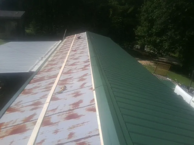 Old rusted panels beside newly installed green metal roofing — Wind Damage Roof Repair by Roofing Brothers in Richmond