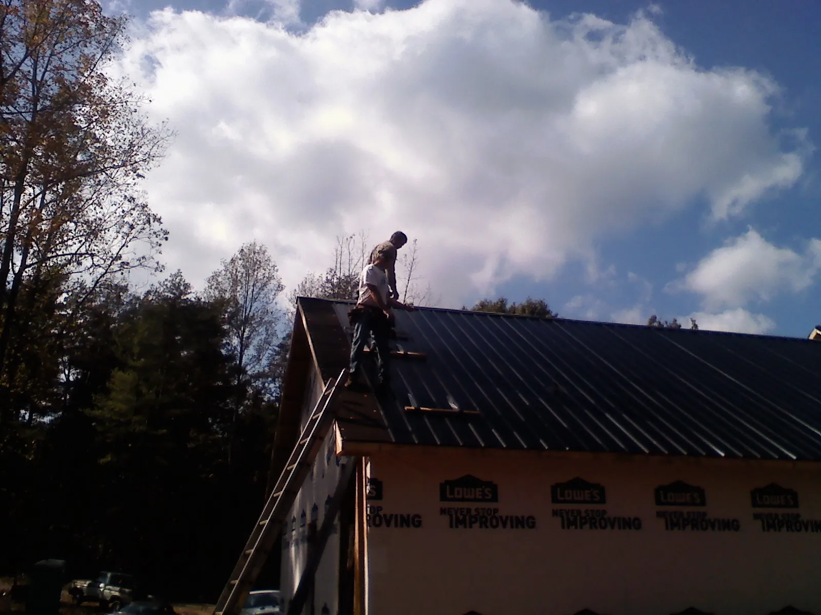 Roofer fastening dark metal panels high against a cloudy sky, from a Roof Inspection job in Richmond